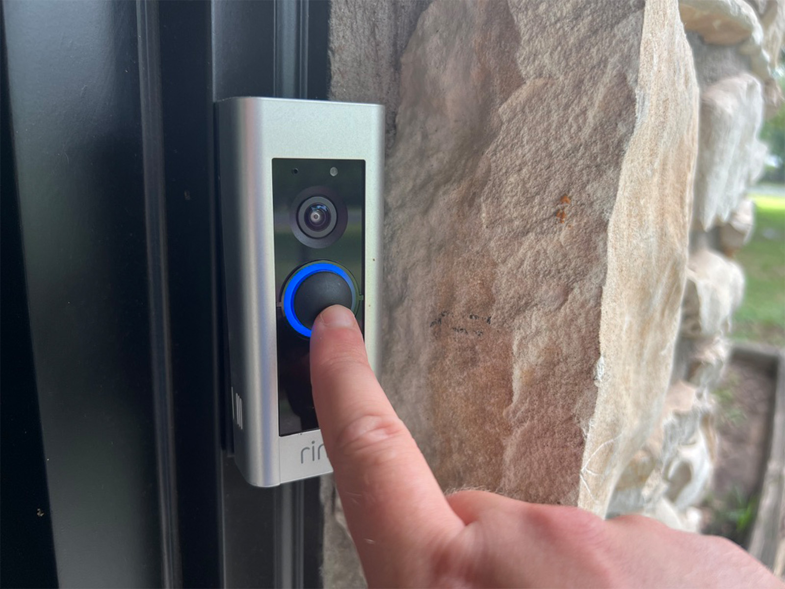 A finger pressing the Ring Video Doorbell Pro's button with the blue ring illuminated