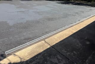 The same transition after sealing, with the coating stopped cleanly at the trench drain and the concrete left untouched