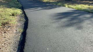 The sealed driveway running along the grass, dark and uniform again