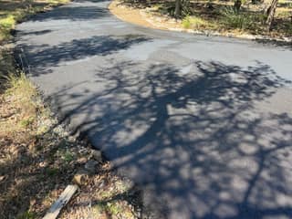 The curve of the driveway partway through sealing, with the coated section dark and the rest still gray