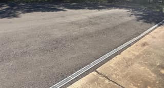 The worn asphalt meeting the concrete slab and trench drain before sealing