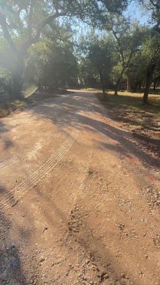 Tire tracks and roller marks pressed into the compacted base under the trees