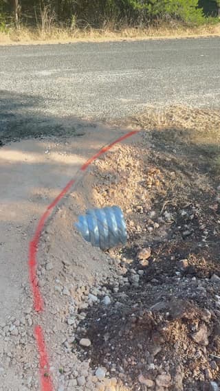 A trench with electrical conduit cut across the driveway base, with a red paint line marking the edge of the paving area