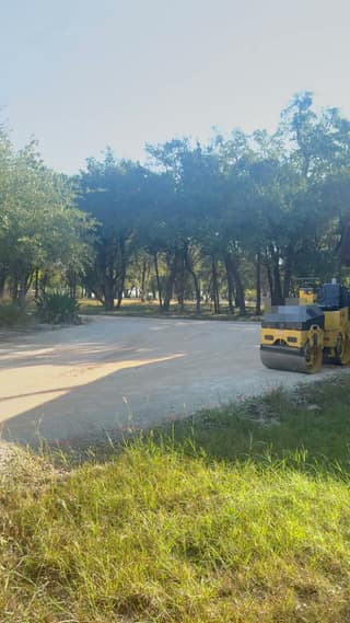 The roller parked on the graded base where the driveway curves around the agave bed