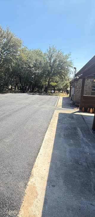 The new asphalt meeting the existing concrete slab beside the house, with a clean compacted edge between the two surfaces