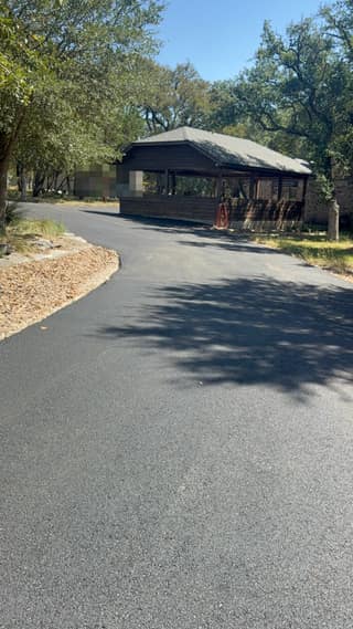 The finished asphalt driveway curving toward the carport, with the edge of the old gravel still visible along the left side