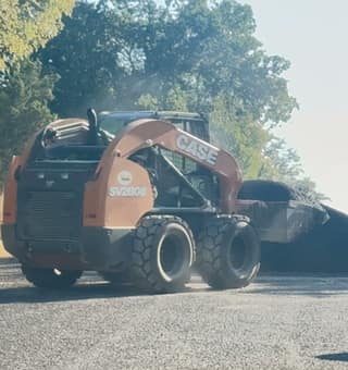 The Case skid steer carrying a bucket of hot-mix asphalt across the freshly paved driveway