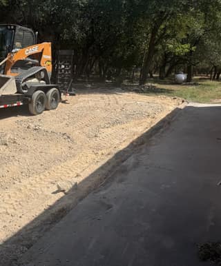 The contractor's Case skid steer on its trailer at the edge of the graded base, with fresh asphalt already down in the foreground