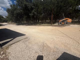 The skid steer spreading fresh road-base material next to the first section of new asphalt