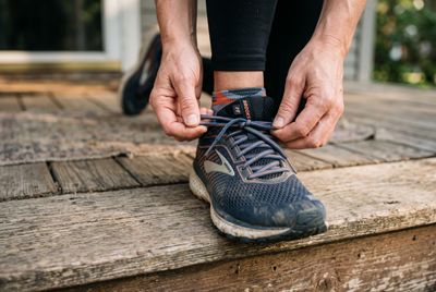 Hands lacing up a running shoe on a doorstep in the morning