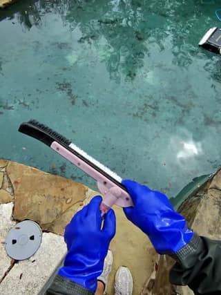 Gloved hands locking a soft pool brush onto a telescopic pole