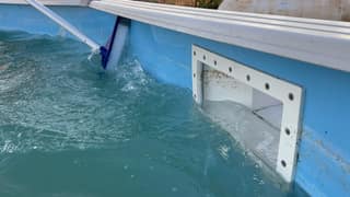 A soft brush cleaning an above-ground liner beside the wall skimmer