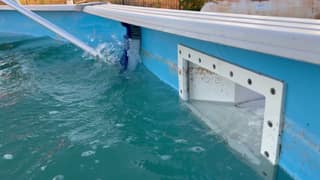 A soft pool brush angled beneath the top rail of an above-ground pool
