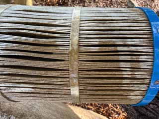 Close-up of a pool filter cartridge during rinsing, with brown debris still visible between some pleats
