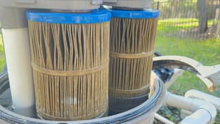 Two dirty pool filter cartridges standing in the tank beside the center standpipe