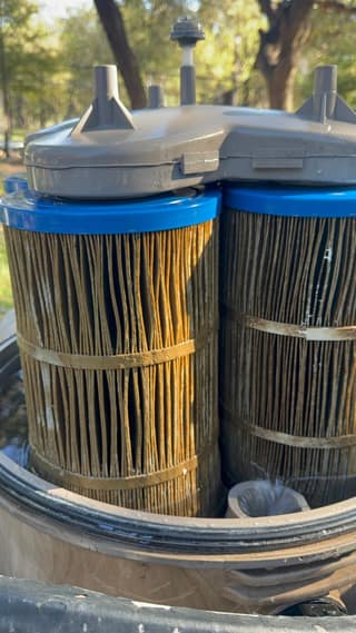 Three dirty brown pool filter cartridges inside an open Hayward filter tank