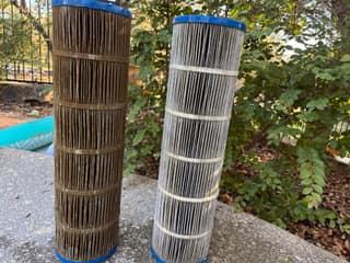 A dirty brown pool filter cartridge standing next to a rinsed, light gray cartridge
