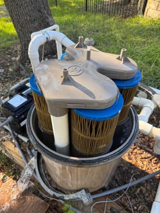 Open Hayward SwimClear filter tank showing three dirty cartridges under the gray top manifold