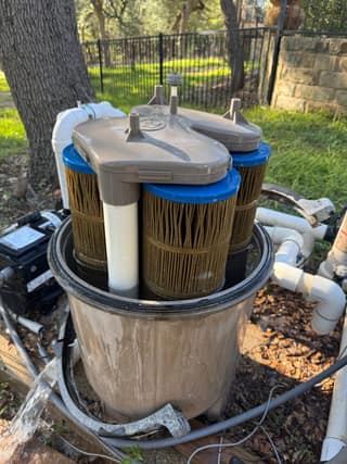 Open SwimClear filter tank with the gray manifold sitting on top of three dirty cartridges