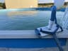 A wheeled manual vacuum head, pole, and hose beside an above-ground pool