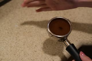 A dosed portafilter on the counter with a hand above it