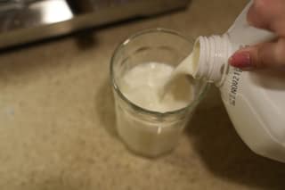 A glass of milk and ice with a jug of whole milk behind it