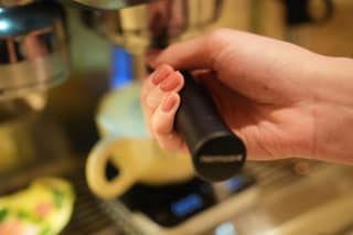 A hand gripping the Normcore bottomless portafilter handle