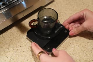 Hands placing a glass cup on the scale on the drip tray