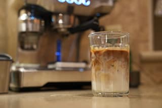 An iced latte in a glass with the Breville Oracle behind it