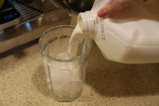 Milk pouring over ice cubes in a tall glass