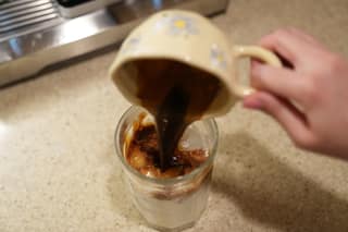 Pouring espresso from the cup into the glass of iced milk