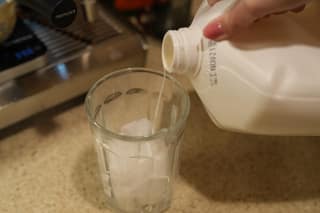 Pouring whole milk into a glass full of ice