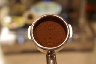 A tamped puck in the portafilter with the machine blurred behind it