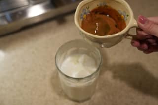 Pouring espresso from the cup over a glass of iced milk