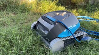 The Dolphin Cayman on the grass after a cleaning cycle, with its cable and float beside it