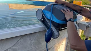 The Dolphin Cayman being lifted over the pool rail with its rubber tracks visible