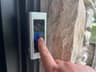 A finger pressing the Ring Video Doorbell Pro's button with the blue ring illuminated
