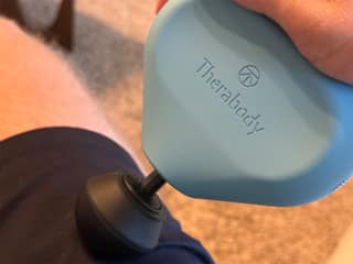The second-generation Theragun Mini held against a thigh