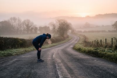 A tired runner resting hands on knees on an empty road at dawn