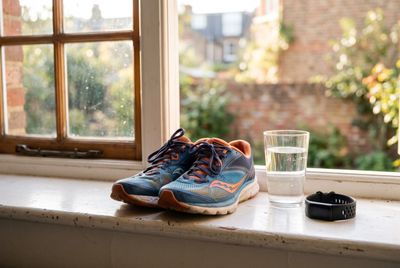 Running shoes, a glass of water and a fitness tracker on a windowsill